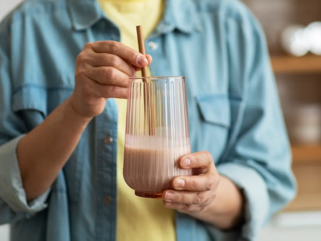 A person holding a ribbed glass of protein shake with a straw