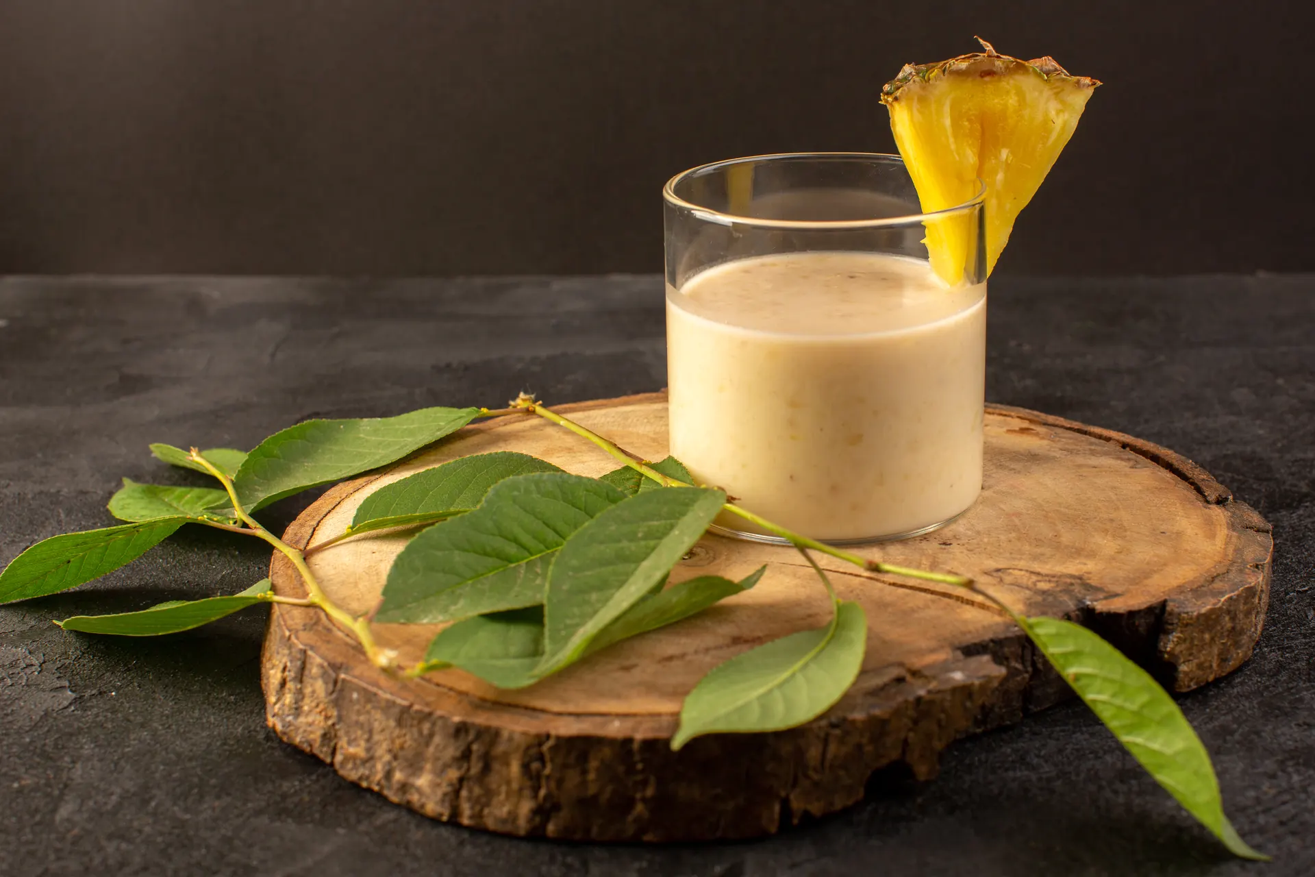 A protein shake in a glass on a wood slice, with pineapple and fresh leaves